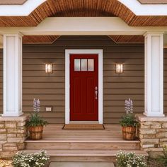 a red front door on a house with two planters and flowers in the foreground