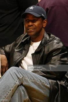 a man in a leather jacket and hat sitting on a bench at a basketball game