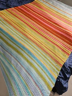 a multicolored crocheted blanket is laying on the floor next to a bed