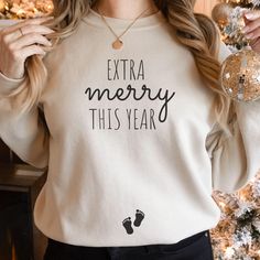 a woman standing in front of a christmas tree wearing a sweatshirt that says extra merry this year