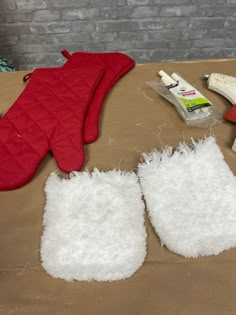 two oven mitts, one red and one white are sitting on a table next to other items