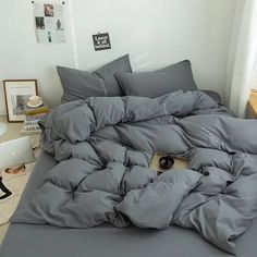 an unmade bed with grey sheets and pillows