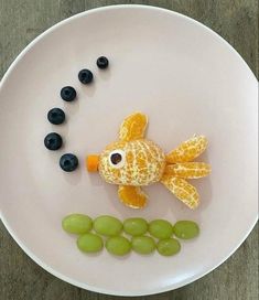 a white plate topped with grapes and a fish made out of oranges, blueberries