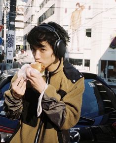 a young man wearing headphones and eating a doughnut on the street in front of a car