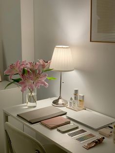 a white desk topped with a lamp next to a vase filled with flowers