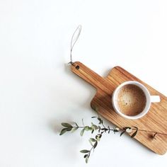 a cup of coffee sitting on top of a wooden cutting board next to a plant