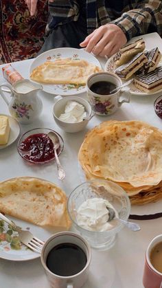 a white table topped with lots of food and cups of coffee next to each other