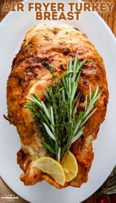 an air fryer turkey breast on a white plate with lemon wedges and rosemary garnish