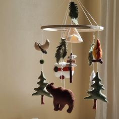 a mobile with animals and trees hanging from it's sides in front of a window