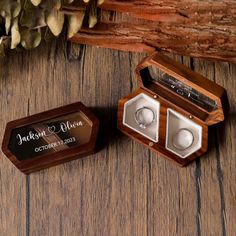 two wooden boxes with wedding rings in them on a table next to some dried flowers