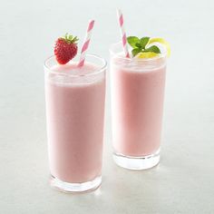 two glasses filled with pink smoothie and strawberries on the top one glass is half full