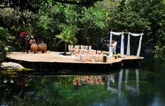 an outdoor wedding set up on a dock in the middle of a lake surrounded by greenery