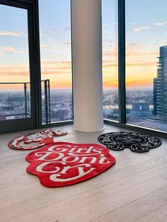 three red and black rugs on the floor in front of large windows with city view