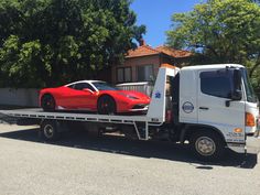 a red sports car is on the back of a tow truck in front of a house