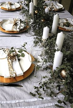 the table is set with white and gold plates, silverware, greenery and candles