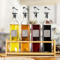 four bottles of different types of oil on a wooden tray in front of some bread