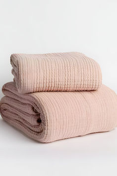 two blankets folded on top of each other in pink and beige colors, sitting side by side against a white background