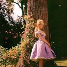 a woman standing next to a tree wearing a purple dress