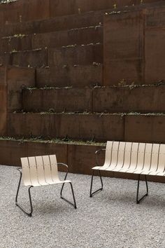 two white chairs sitting next to each other in front of a wall with plants growing on it