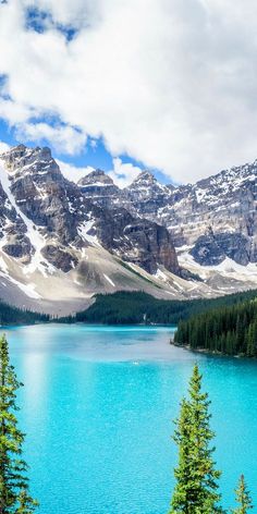 the mountains are covered in snow and have blue water surrounded by pine trees on either side