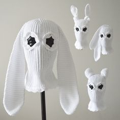 three white knitted hats with black eyes and ears on top of a wooden stand