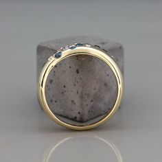 a yellow gold wedding ring with blue sapphires on the outside and inside, sitting on top of a stone block