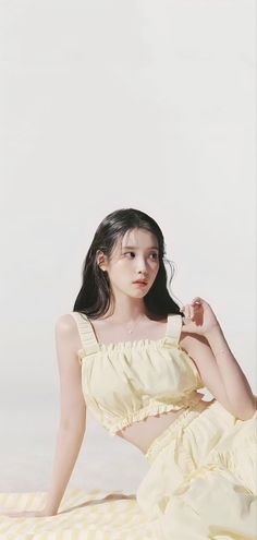 a young woman sitting on top of a bed wearing a yellow dress and posing for the camera