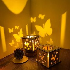 two lit candles sitting on top of a table next to a pine cone and paper butterflies