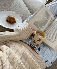 a person sitting on a couch reading a book and holding a cup of coffee in their lap