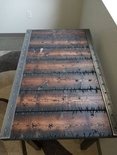 a wooden table with barbed wire on the top and metal frame at the bottom, in front of a window