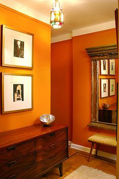 an orange room with pictures on the wall and a wooden dresser in front of it