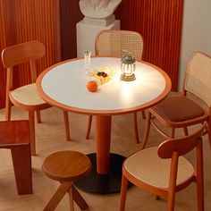 a white table with four chairs around it and a vase filled with fruit on top