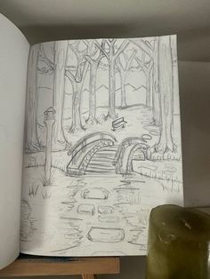 an open book with a drawing of a bridge in the woods