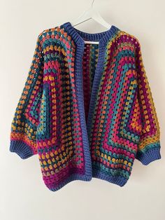 a colorful crocheted sweater hanging on a white hanger with the back turned down