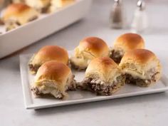 mini cheeseburger sliders on a white plate next to a baking pan with more sliders in the background