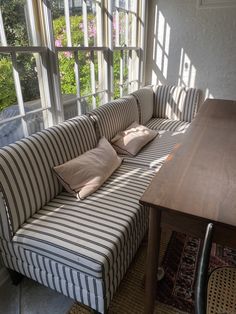 a striped couch with pillows on it in front of a table and large open window