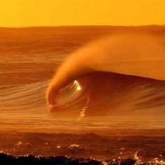 a large wave in the ocean at sunset