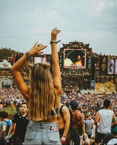 a woman standing in front of a crowd at a music festival with her hands up