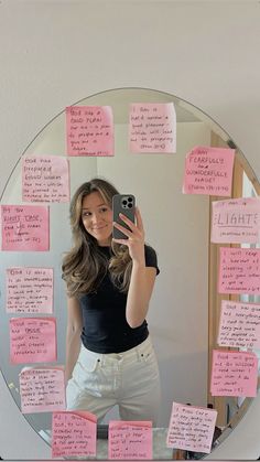 a woman taking a selfie in front of a mirror with sticky notes on it