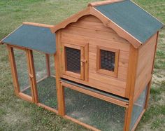 a large wooden chicken coop with two doors and windows on the roof, sitting in grass