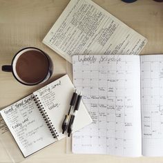 a cup of coffee, notebook and pen on a wooden table with notes in it