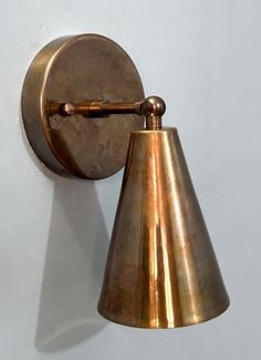 an antique brass wall light on a white wall with a small cone shade hanging from it's side