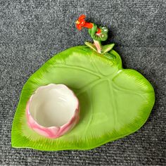 a frog figurine sitting on top of a green leaf shaped plate with a bowl in it