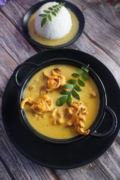 two black plates filled with food on top of a wooden table next to white rice