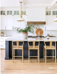 a kitchen with white cabinets and black island in the center is surrounded by three chairs