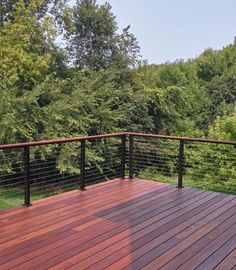 a wooden deck with metal railing and trees in the background