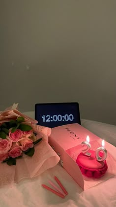 a bouquet of pink roses sitting next to a birthday cake with candles on it and an electronic clock