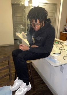 a man with dreadlocks sitting on top of a counter using a tablet computer