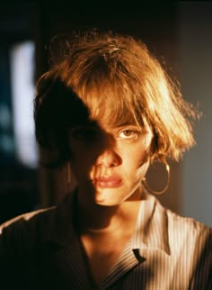 a close up of a person with short hair and earrings on her head, looking at the camera