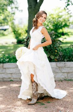 a woman in a white dress and cowboy boots posing for the camera with her bouquet